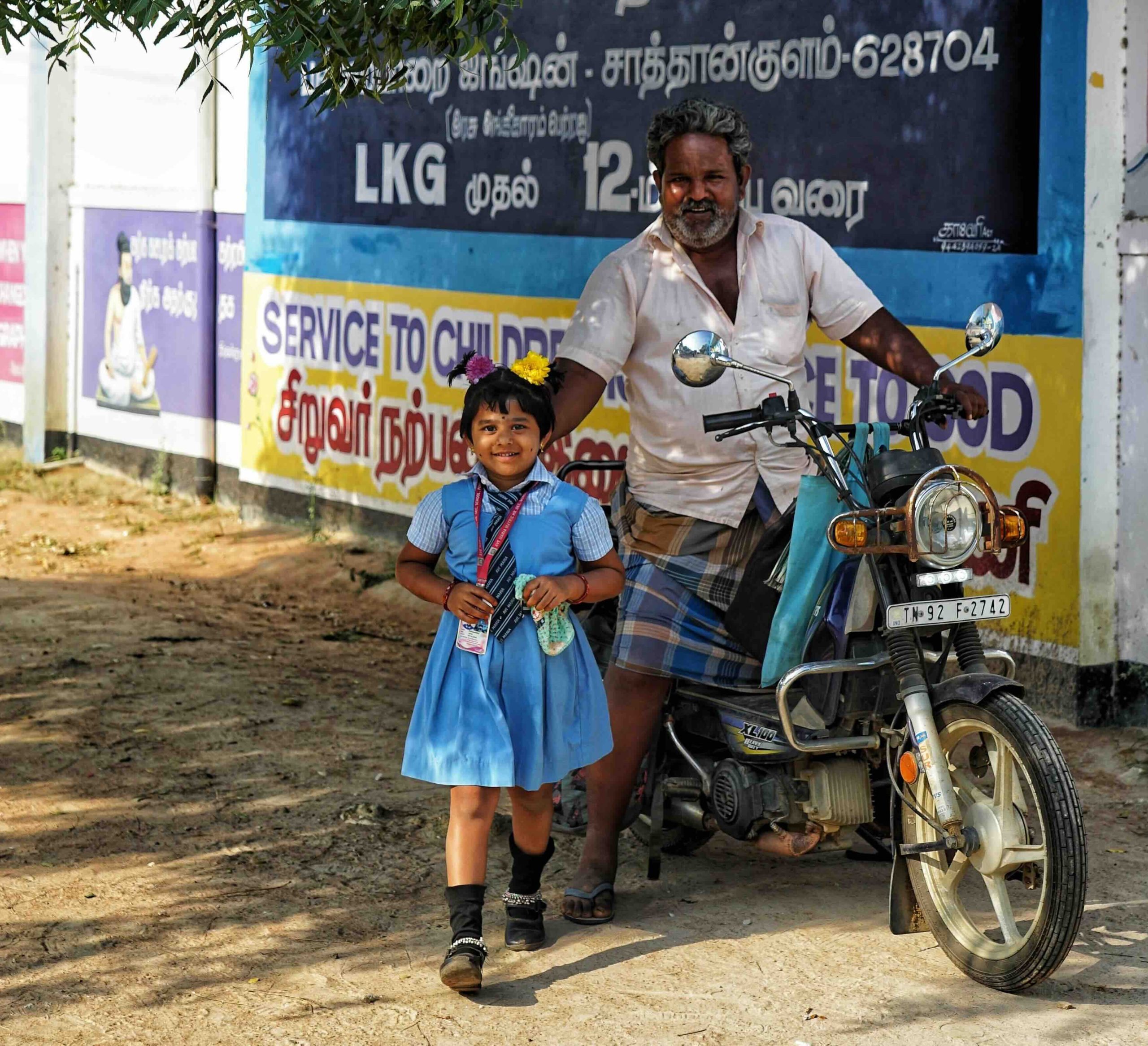 Primary student arriving at school with her father on a motorbike