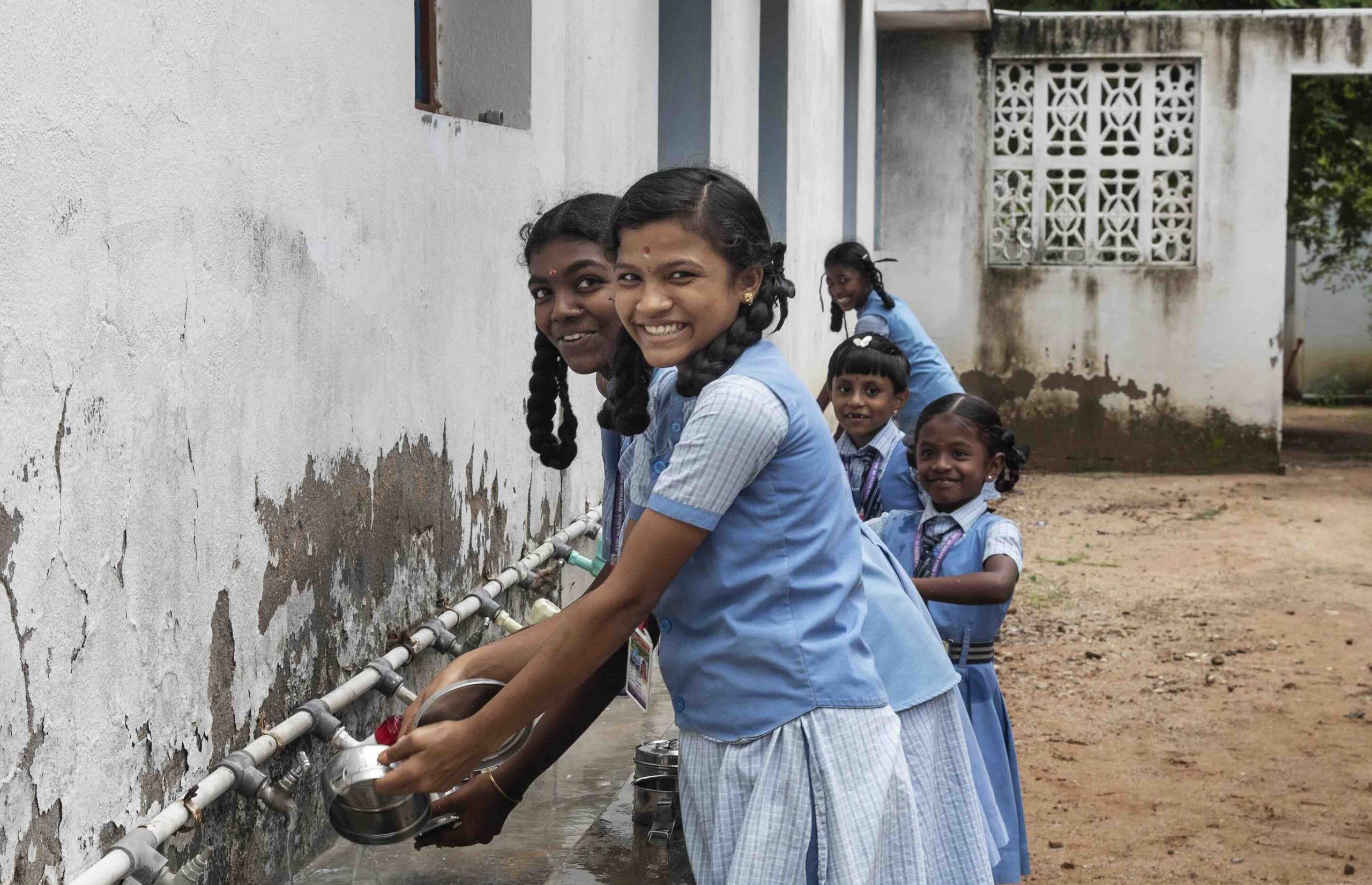 Smiling students washing their lunchboxes after the lunch break
